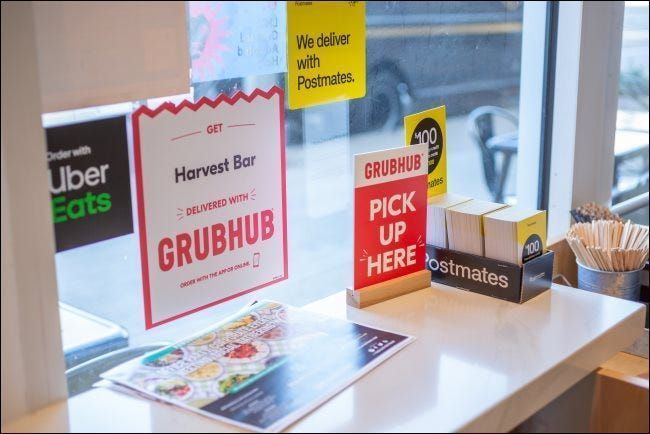 Πινακίδες για GrubHub, Postmates και Uber Eats σε ένα εστιατόριο.