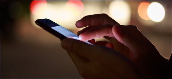 Un primo piano delle mani utilizzando uno smartphone di notte per strada.
