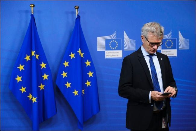 ایک آدمی اسمارٹ فون استعمال کر رہا ہے جس کے پیچھے یورپی یونین کے دو جھنڈے ہیں۔