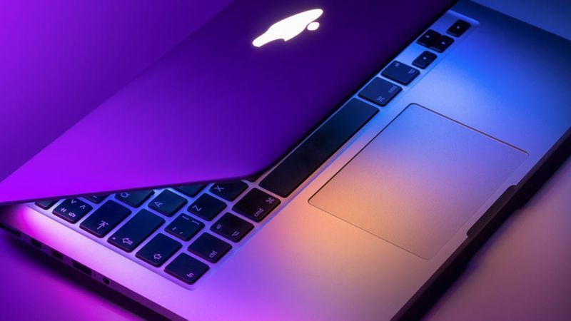 MacBook Pro daļēji atvērts purpursarkanā un zilā krāsā