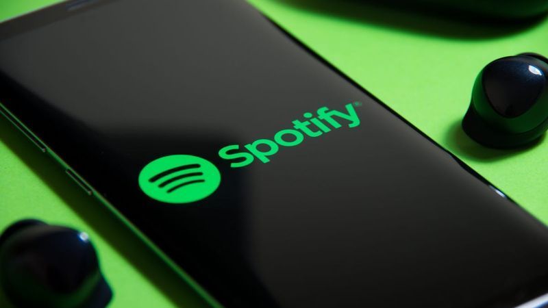 يظهر الهاتف الذكي شعار Spotify بجوار سماعات الأذن اللاسلكية على خلفية خضراء.
