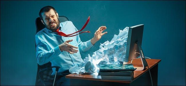 Mladi naglašeni zgodan poslovni čovjek koji radi za stolom u modernom uredu, viče na zaslon prijenosnog računala i ljuti se zbog neželjene e-pošte. Kolaž s brdom zgužvanog papira.