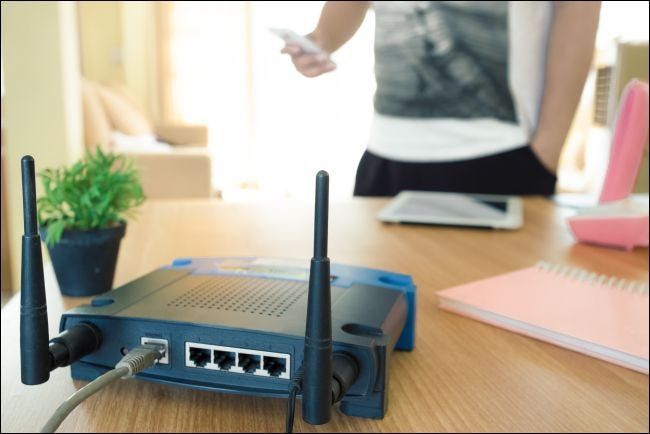 primo piano di un router wireless e un giovane che utilizza uno smartphone nel soggiorno di casa con una finestra sullo sfondo