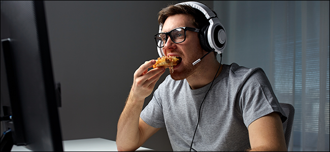 Seorang lelaki duduk di hadapan komputer, memakai set kepala, dan makan piza.
