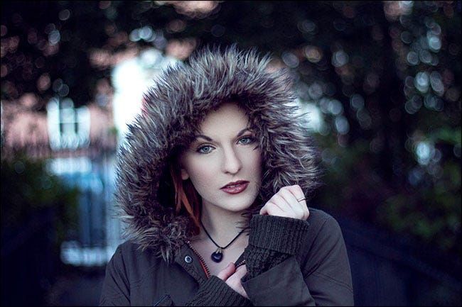 Un ritratto di una donna che indossa un cappotto con cappuccio foderato di pelliccia in cui lo sfondo è sfocato.